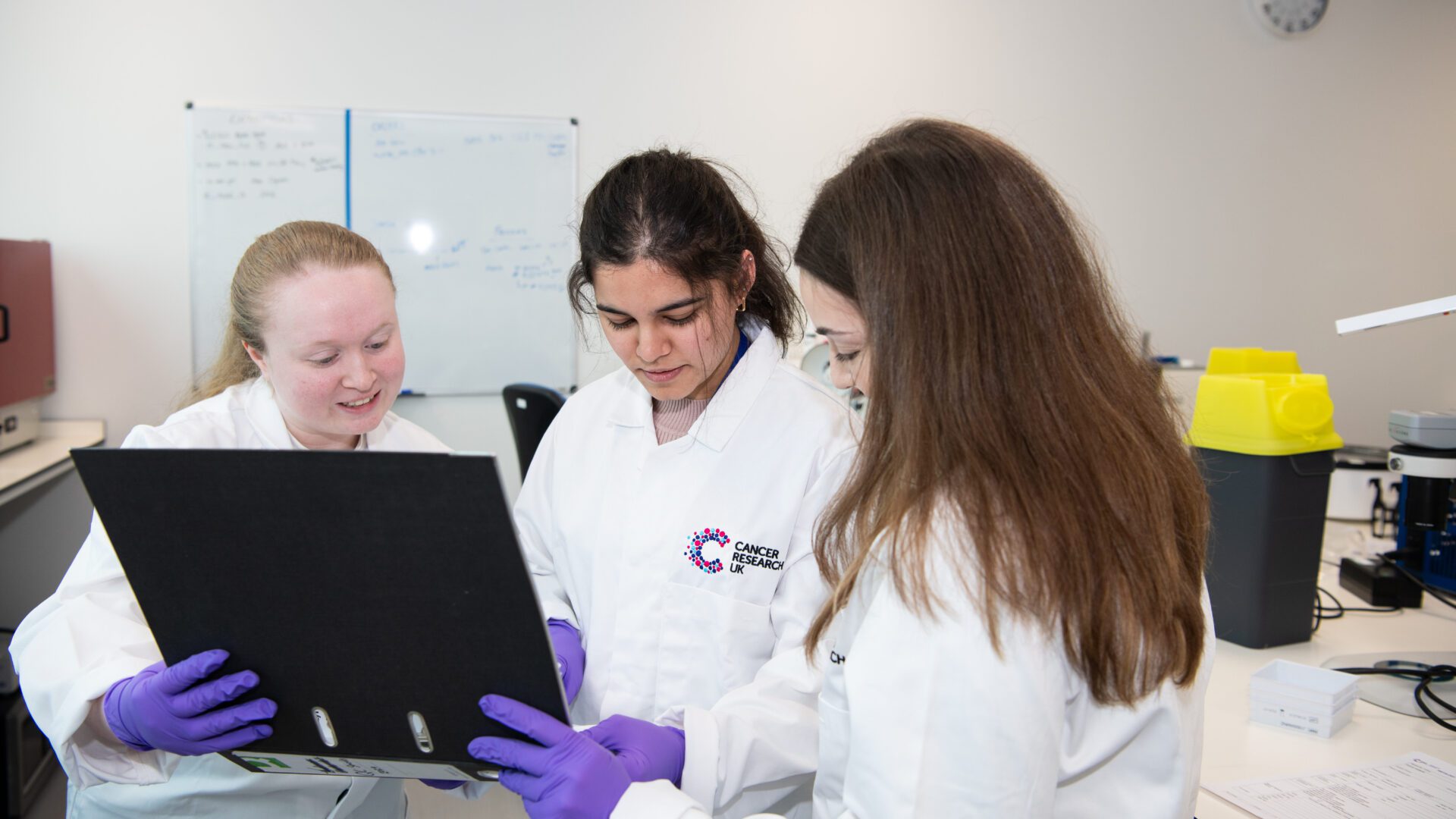 Three researchers in lab coats looking at documentation in a laboratory space