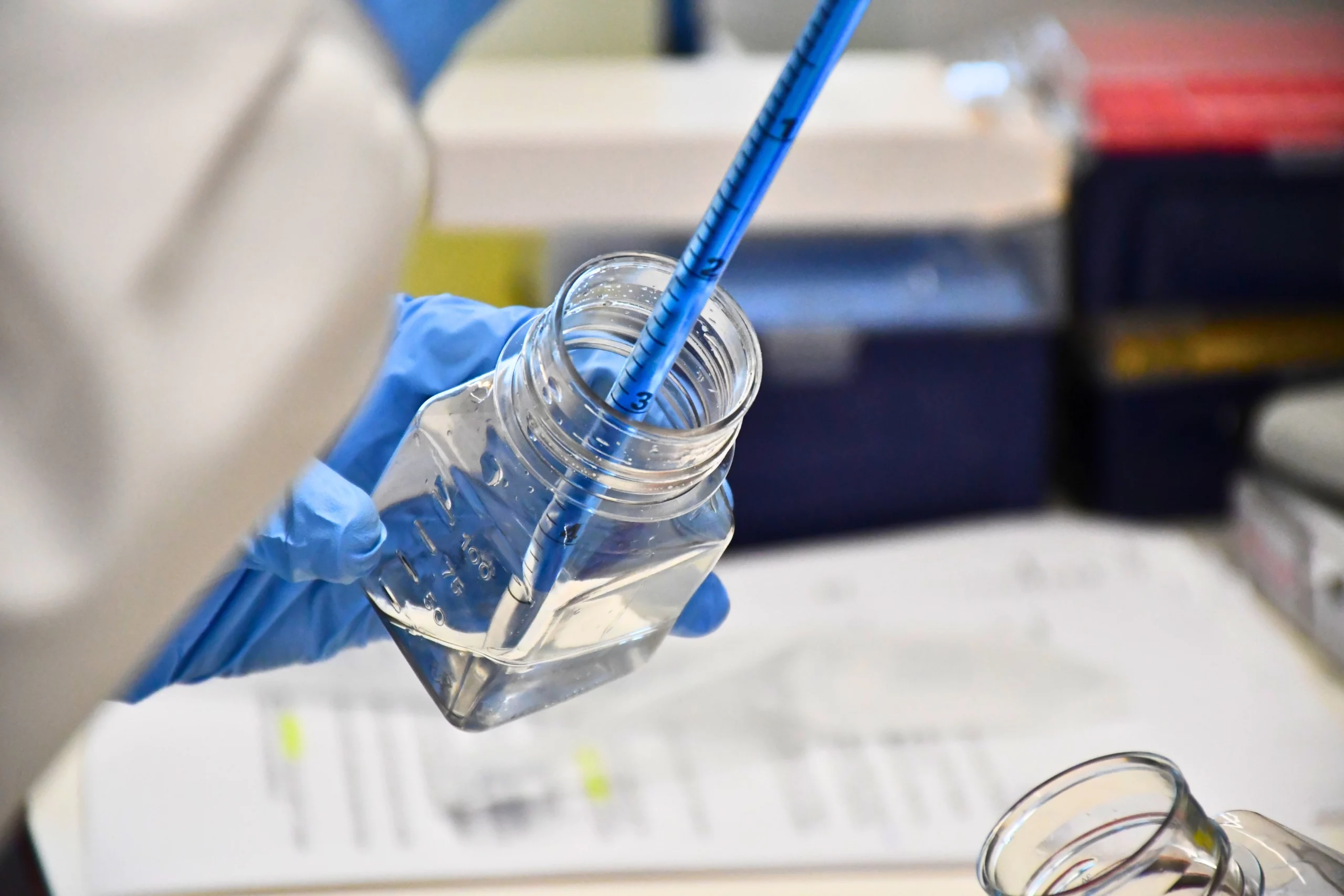 Gloved hands filling a stripette white lab coat
