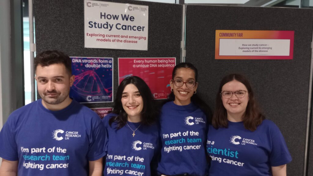 Photograph of four researchers in matching Cancer Research UK t-shirts in front of display stands